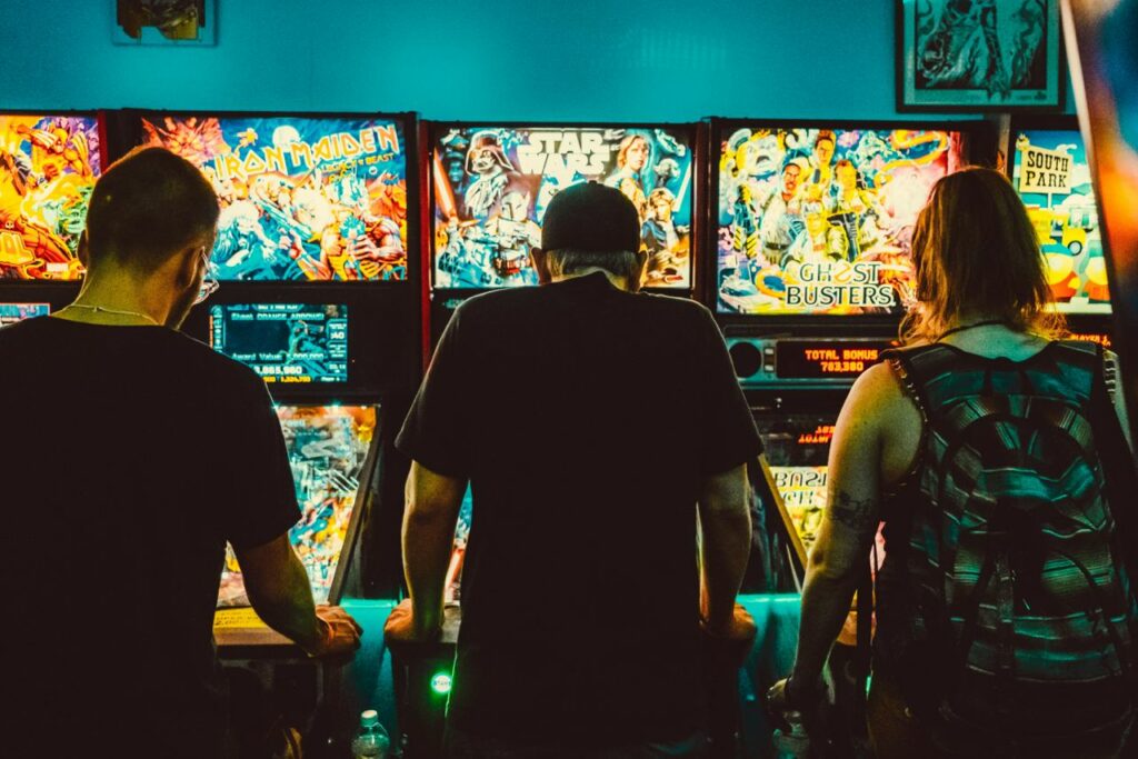 three people playing arcade games in a game club, shot from behind the back